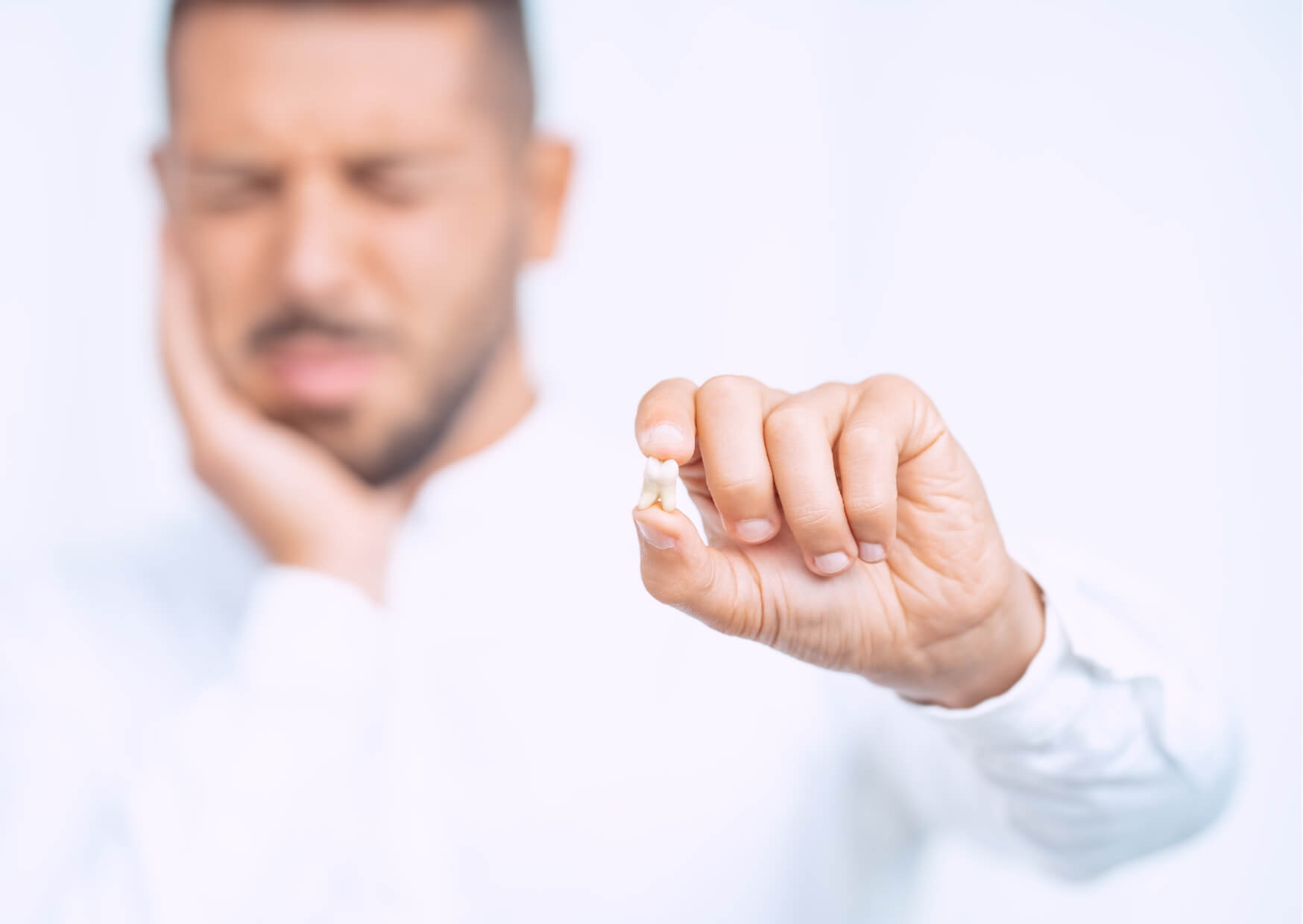 Man holding an extracted damaged tooth while experiencing tooth pain, illustrating common signs of a cracked tooth.