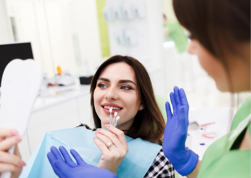 Dentist showing veneer shade samples during a cosmetic consultation while explaining how veneers cost can vary by location and treatment needs.